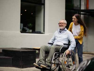 Daughter and disabled father in wheelchair go for a walk. Paralyzed people and disability, handicap overcoming. Handicapped male person and young female guardian in public place